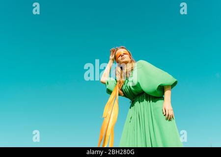 Junge Frau mit verbundenen Augen in einem grünen Kleid unter blauem Himmel Stockfoto