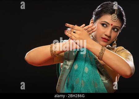 Kathak Tänzerin sitzt anmutig vor einem dunklen Hintergrund. Stockfoto
