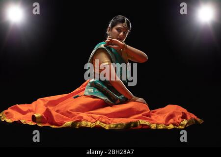 Kathak Tänzerin sitzt anmutig vor einem dunklen Hintergrund. Stockfoto