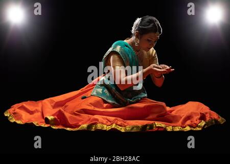 Kathak Tänzerin sitzt anmutig vor einem dunklen Hintergrund. Stockfoto