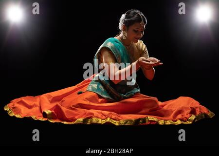 Kathak Tänzerin sitzt anmutig vor einem dunklen Hintergrund. Stockfoto