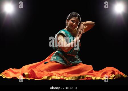 Kathak Tänzerin sitzt anmutig vor einem dunklen Hintergrund. Stockfoto