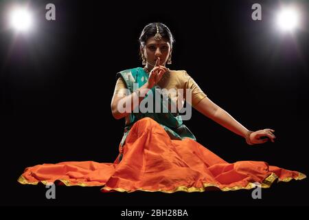 Kathak Tänzerin sitzt anmutig vor einem dunklen Hintergrund. Stockfoto