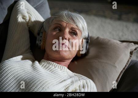 Porträt einer älteren Frau, die sich auf der Couch entspannt und Musik mit Kopfhörern hört Stockfoto