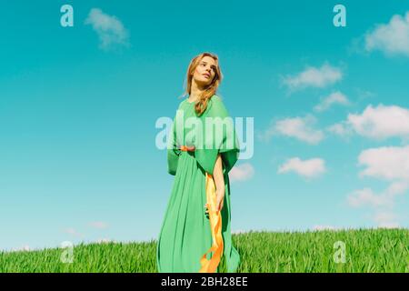 Junge Frau trägt ein grünes Kleid auf einem Feld mit Bändern um ihre Taille gewickelt stehen Stockfoto