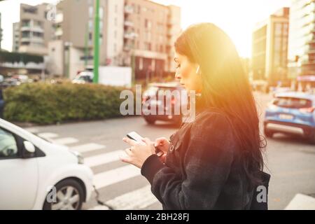Schöne Frau, die mit dem Smartphone auf einer Straße steht Stockfoto