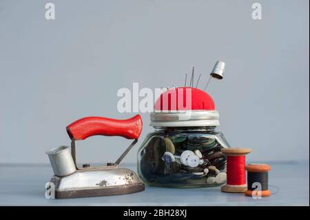 Einmachglas mit Näh-Tasten, Pin-Kissen, Spulen aus Faden, Handflink und Retro-Eisen Stockfoto