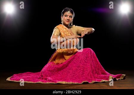 Kathak Tänzerin sitzt anmutig und tritt vor einem dunklen Hintergrund auf. Stockfoto