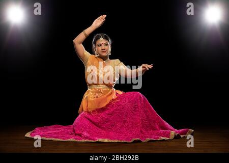 Kathak Tänzerin sitzt anmutig und tritt vor einem dunklen Hintergrund auf. Stockfoto
