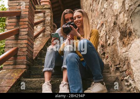 Zwei junge Frauen, die auf Treppen sitzen und die Kamera betrachten, Greve in Chianti, Toskana, Italien Stockfoto