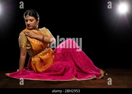 Kathak Tänzerin sitzt anmutig und tritt vor einem dunklen Hintergrund auf. Stockfoto