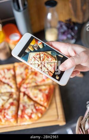 Frau Hand Foto von hausgemachter Pizza mit Smartphone Stockfoto