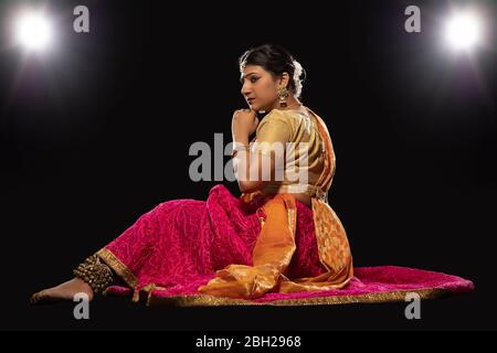 Kathak Tänzerin sitzt anmutig und tritt vor einem dunklen Hintergrund auf. Stockfoto
