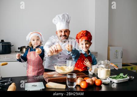 Portrait des Vaters mit zwei Kindern, die in der Küche zu Hause Teig zubereiten Stockfoto