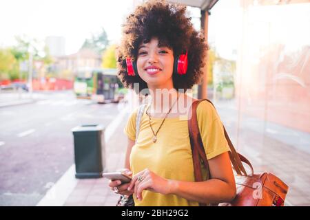 Glückliche junge Frau mit Afro-Frisur Musik mit Kopfhörern in der Stadt hören Stockfoto