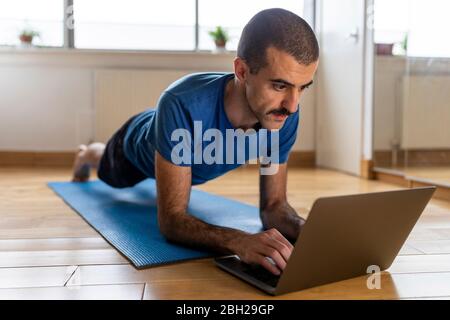 Mann, der eine Planke macht und Laptop zu Hause benutzt Stockfoto