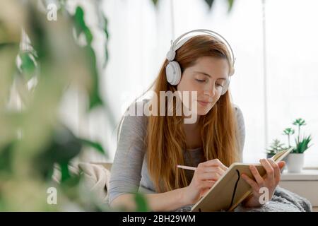 Junge Frau mit Kopfhörern und Notizen zu Hause Stockfoto