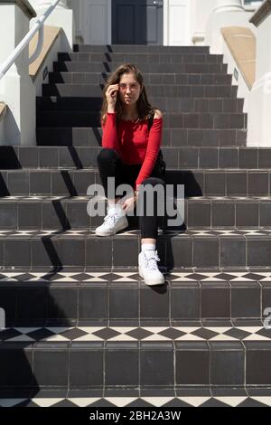 Portrait einer jungen Frau, die auf der Treppe am Hauseingang sitzt Stockfoto