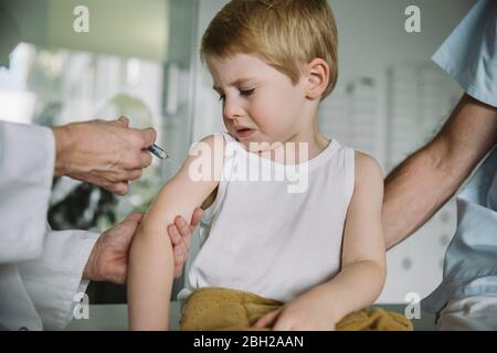 Kinderarzt injiziert Impfstoff in den Arm des unglücklichen Kleinkindes Stockfoto