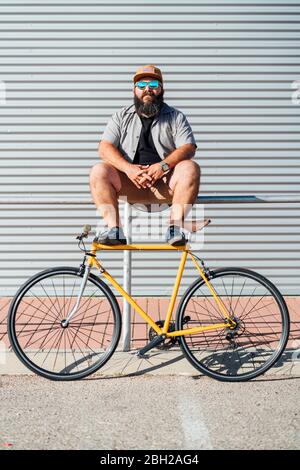 Porträt von bärtigen Mann mit gelben Fixie Fahrrad auf Geländer sitzen Stockfoto