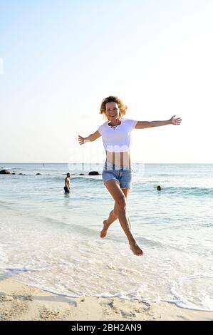 Schöne Frau läuft und springt vor Freude am Strand Stockfoto