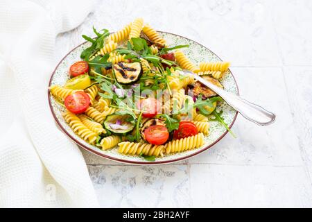 Teller mit vegetarischen Nudelsalat mit gegrillten Zucchini, Tomaten, Rucola, roten Zwiebeln und Balsamico-Essig Stockfoto