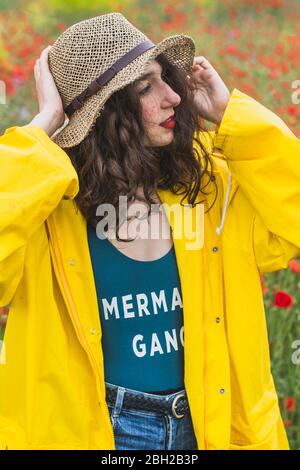 Portrait einer jungen Frau mit Hut und gelber Regenjacke auf Blumenwiese Stockfoto