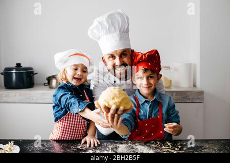 Portrait des Vaters mit zwei Kindern, die in der Küche zu Hause Teig zubereiten Stockfoto