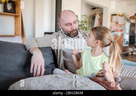 Vater und kleine Tochter sitzen zusammen auf der Couch zu Hause Spaß haben Stockfoto