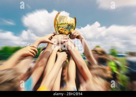 Gruppe von Kindern feiern Sport Erfolg im Freien. Boys Holding und Rising Golden Trophy zusammen. Fußballmannschaft Hält Den Goldenen Cup Auf Stockfoto