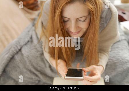 Junge Frau, die mit dem Smartphone auf der Decke liegt Stockfoto