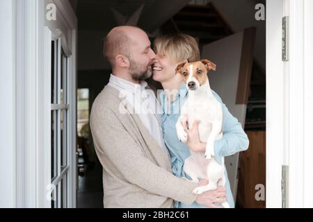 Glückliches Paar mit Hund küssen am Eingang ihres Hauses Stockfoto