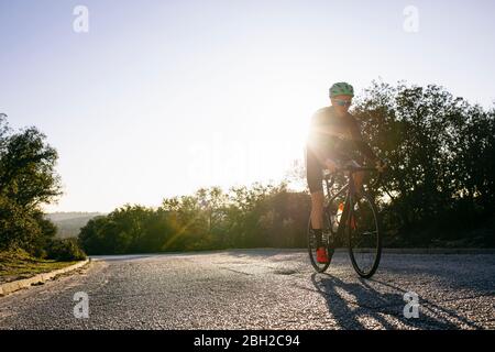 Sportler, die bei Sonnenuntergang Fahrrad auf der Landstraße fahren Stockfoto