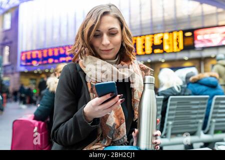 Frau, die am Bahnhof sitzt und das Handy benutzt Stockfoto