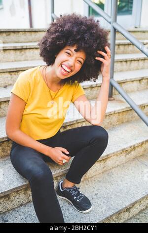 Porträt einer lachenden jungen Frau, die draußen auf einer Treppe sitzt