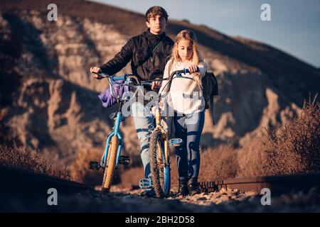 Junge und Mädchen zu Fuß mit Fahrrädern in ländlicher Landschaft Stockfoto