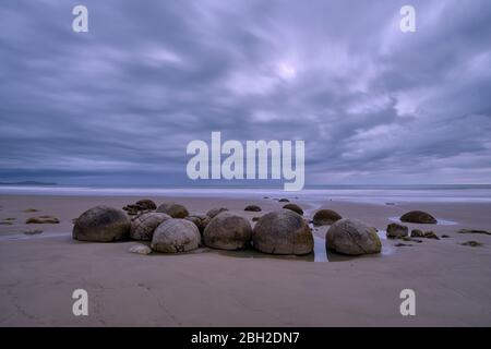 Neuseeland, Otago, Moeraki, lange Wolkenbedeckung über Moeraki-Felsbrocken am Koekohe Beach in der Abenddämmerung Stockfoto