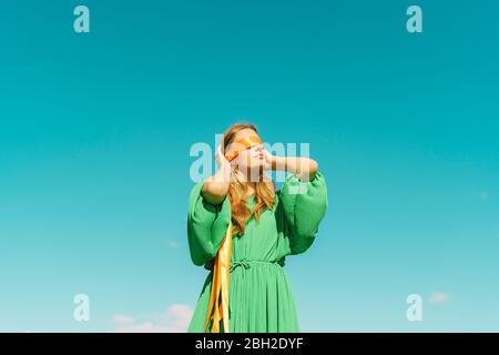 Junge Frau mit verbundenen Augen in einem grünen Kleid unter blauem Himmel Stockfoto