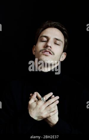 Porträt eines jungen Mannes mit geschlossenen Augen vor schwarzem Hintergrund Stockfoto