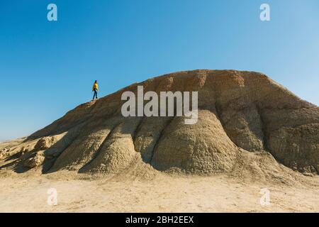 Frau, die auf einem Hügel in der desertischen Landschaft von Bardenas Reales, Arguedas, Navarra, Spanien, spazierengeht Stockfoto