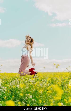 Glückliche junge Frau, die im Frühling auf einer Blumenwiese springt Stockfoto