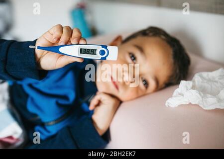 Porträt eines kranken kleinen Jungen im Bett liegend mit digitalem Thermometer Stockfoto