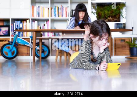Mädchen und ihre Schwester im Hintergrund mit elektronischen Geräten zu Hause Stockfoto