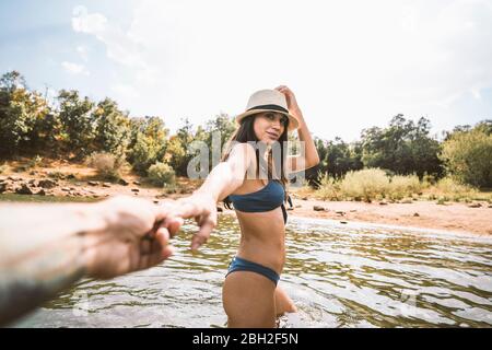 Porträt einer jungen Frau, die in einem See watend und die Hand ihres Freundes hält Stockfoto