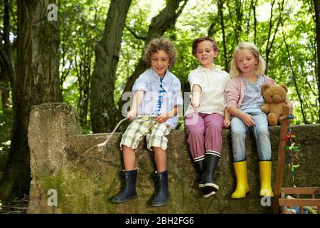 Kinder sitzen auf Steinmauer im Wald Stockfoto