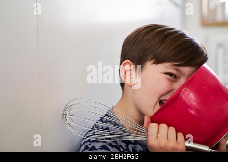 Portrait des Jungen mit roter Rührschüssel und Eierbesen in der Küche Stockfoto