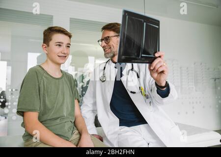 Arzt erklärt Röntgenbild der gebrochenen Hand zu Teenager Jungen in der medizinischen Praxis Stockfoto