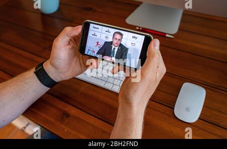 Warendorf, Deutschland. April 2020. Ein Mann schaut auf das Display seines Smartphones, Dies zeigt Tim Meyer, Chief Medical Officer des Deutschen Fußballverbandes (DFB) und Leiter der Task Force Sportmedizin/Special Game Operations der Deutschen Fußball-Liga (DFL), während einer Live-Video-Pressekonferenz nach der DFL-Mitgliederversammlung zu den Folgen der Corona-Pandemie. Kredit: Guido Kirchner/dpa/Alamy Live News Stockfoto