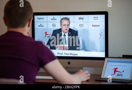 Warendorf, Deutschland. April 2020. Ein Mann schaut auf den Monitor seines Computers, auf dem Tim Meyer, Chefarzter des Deutschen Fußballverbandes (DFB) und Leiter der Task Force Sportmedizin/Special Game Operations der Deutschen Fußball-Liga (DFL), Zu sehen ist während einer Live-Video-Pressekonferenz nach der Hauptversammlung der DFL über die Folgen der Corona-Pandemie. Kredit: Guido Kirchner/dpa/Alamy Live News Stockfoto