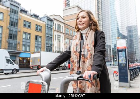 Glückliche Frau in der Stadt mit Leihrad, London, Großbritannien Stockfoto